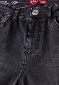 Jean slim gris foncé avec bouton en métal et poches cousues, affichant les étiquettes de ceinture "Slim Fit" et "Your Denim."