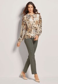 Blouse met luipaardprint en een striknekdetail, lange mouwen en gathered manchetten, gecombineerd met olijfgroene getsailleerde broek en nude hoge hakken.