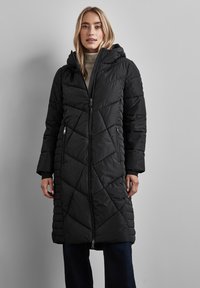 Svart puffjacka med dragkedjestängning, huva och diagonalt quiltat mönster. Har sidofickor och långa ärmar. Mjuk textur.