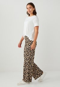Witte t-shirt met korte mouwen gecombineerd met losse broek met luipaardprint. De broek heeft een dierenprint in beige en zwarte tinten. Witte sneakers.