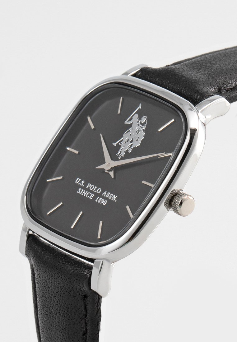 Schwarze rechteckige Uhr mit einem silbernen Metallgehäuse, schwarzem Ziffernblatt, silbernen Stundenmarkierungen, Logodesign und einem strukturierten schwarzen Lederarmband.