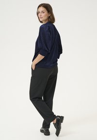 Top in velluto a coste blu navy con maniche a sbuffo, abbinato a pantaloni neri larghi e scarpe con platform nere, con le mani nelle tasche.
