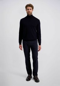 Marineblauer Rollkragenpullover und dunkle Hose. Der Pullover hat eine glatte Textur und ein tailliertes Design. Das Outfit wird mit dunklen Slippern kombiniert.