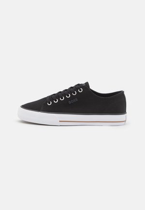 Black low-top canvas sneaker with white rubber sole, brown stripe, black laces, and "BOSS" logo on side and tongue.