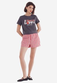 T-shirt gris à manches courtes avec un graphisme "Cherry Love", associé à un short à carreaux rouge et blanc. Des chaussures plates noires complètent la tenue.
