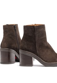 Brown suede ankle boots with a zip closure, block heel, and contrasting white stitching along the sole. Soft texture and modern design.