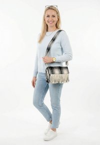 Naine helesinisest kampsunist ja teksadest, kandes musta-valget ääristatud õlakotti, valged tossud ja kuldne käekell.