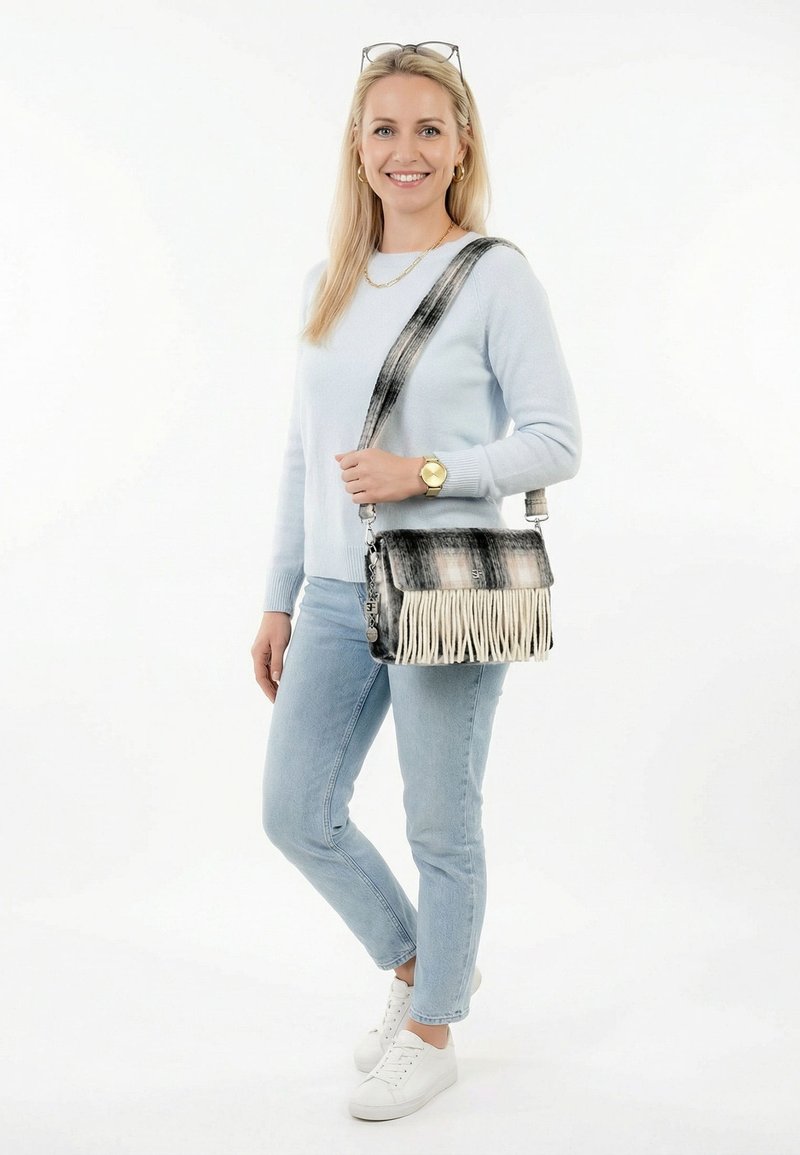 Naine helesinisest kampsunist ja teksadest, kandes musta-valget ääristatud õlakotti, valged tossud ja kuldne käekell.