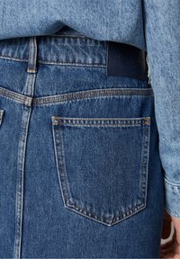 Jeanskjol i medelblått med synlig sömnad och en solid bakfick på höger sida. Har en märkesläderetikett vid midjan.