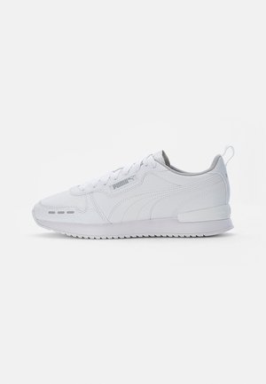 Baskets blanches Puma avec lacets, design cousu, logo sur le côté et semelle texturée vues de l’extérieur sur fond blanc.
