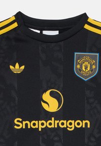 Fekete Manchester United focimez sárga Adidas logóval, sárga Snapdragon szponzor logóval és diszkrét klubcímer mintával az anyagon.