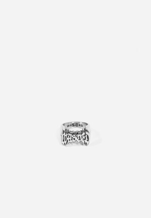 Bague en métal argenté avec un design audacieux et en zigzag, comportant des lettres découpées. Intérieur gravé du mot "WASTED". Texture lisse.
