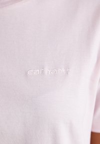 Šviesiai rožinė medvilninė marškinėliai su apvaliu kaklu ir siuvinėtu baltu "carhartt" logotipu kairiajame krūtinės regione. Minkšta tekstūra, kasdienis dizainas.
