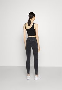 Svart beskuren linne med tunna band, parat med högmidjade, mörkgrå tights och vita sneakers. Slät struktur och åtsittande design.