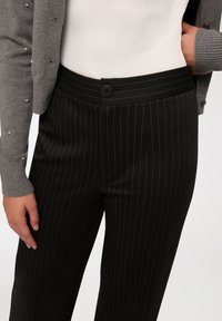 Czarne spodnie w paski z wysokim stanem, z pojedynczym zapięciem na guzik. Połączone z szarym kardiganem z perłowymi zdobieniami.