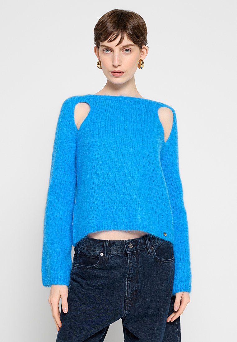 Maglione blu accorciato realizzato in materiale morbido e peloso, con spalle scoperte, maniche lunghe e una vestibilità comoda. Dettaglio hardware dorato di rilievo.