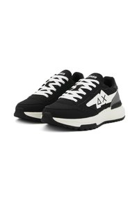 Scarpe sportive in bianco e nero con tomaia in tessuto testurizzato, lacci bianchi e suola ammortizzata; presentano un logo e dettagli di design angolari.