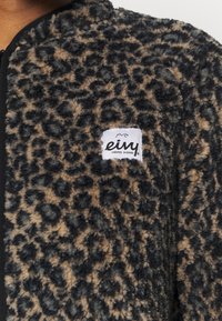 Veste duveteuse imprimé léopard marron et noir avec une étiquette blanche indiquant "eivy UNBORED ONBOARD" sur la poitrine.