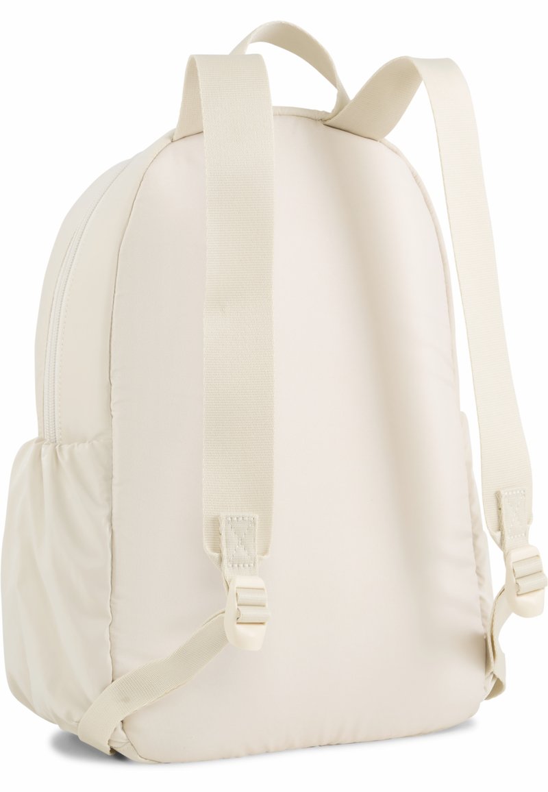 Mochila color crema con tela acolchada, dos correas ajustables y un compartimento principal con cremallera. Textura suave y forma redondeada.