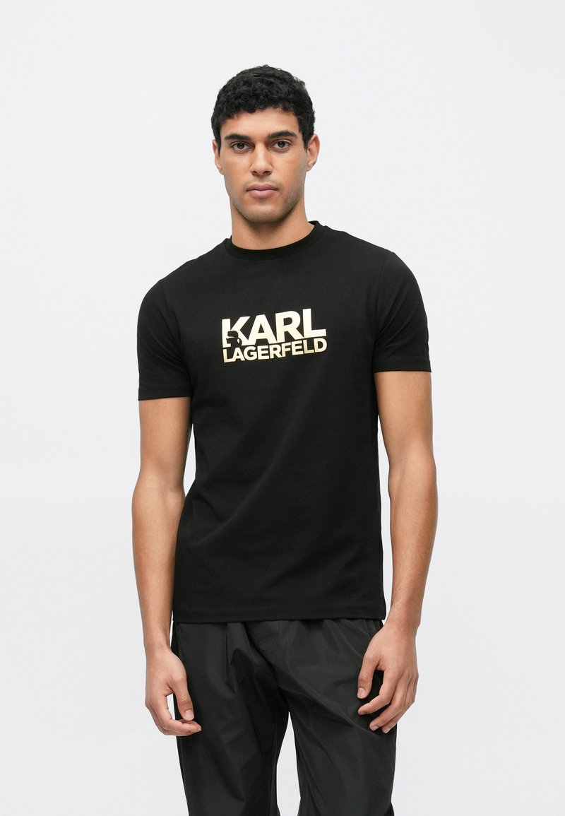 Camiseta negra de algodón con cuello redondo clásico, con el logo dorado "KARL LAGERFELD" impreso en el frente. Manga corta, diseño ajustado.