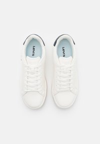 Hvite sneakers laget av syntetisk lær, med flate snørebånd, en blå innersåle og en mørk marineblå aksent på hælen. Levi's-logo på tungen.