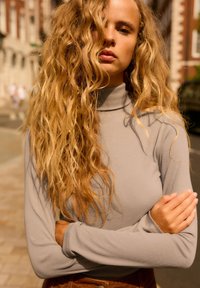 Długi rękaw, jasnoszary, prążkowany top z wysokim kołnierzem. Materiał wydaje się mieć fakturę, w zestawieniu z dolną częścią w ciepłym odcieniu, przypominającą zamsz.