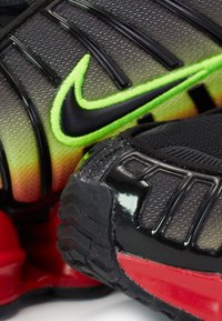 Nike urheilukengät, joissa on gradienttiverkko-yläosa, mustat ja neonvihreät yksityiskohdat, teksturoitu viimeistely ja punamusta kumipohja.