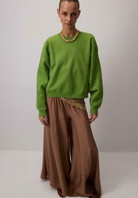 Zelena prevelika majica s širokimi rjavimi hlačami, z vzorčastim poudarkom na pasu. Model nosi ogrlico iz perlic.