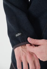 Musta tekstuuriga jakk, millel on sobituv mansett. Varrukas on varustatud nähtava logo sildiga "NORTH BEND" ning lukuga esiosa.