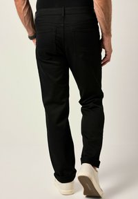 Vaqueros negros con corte recto, que cuentan con dos bolsillos traseros y puños remangados. Llevados con zapatos blancos. Textura de tela suave.