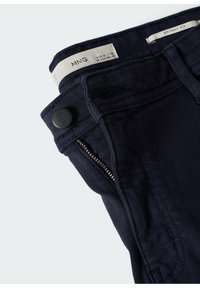 Slim fit tmavě modré džíny z denimu. Mají zipovou kapsu a zapínání na knoflík v pase, hladký povrch a bez vzorů.
