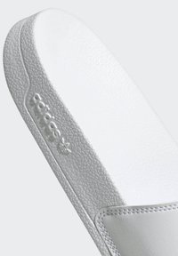 Adidas white slide sandal featuring a textured rubber sole and smooth strap with embossed logo. Clean design, primarily solid color.