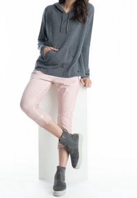 Felpa grigia con tasca frontale e cordino. Pantaloni cropped rosa chiaro con cuciture bianche. Stivaletti grigi alla caviglia con finitura texturizzata.