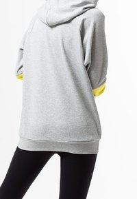 Sweat à capuche gris avec une grande capuche, doté de manches courtes avec des accents jaune vif. Fabriqué en tissu doux, avec un ourlet et des poignets côtelés.