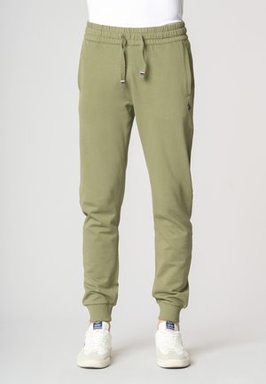 Pantaloni jogger verde oliva con vita elastica, cordoncino, tasche laterali e polsini a costine. Abbinati a sneakers bianche e grigie.