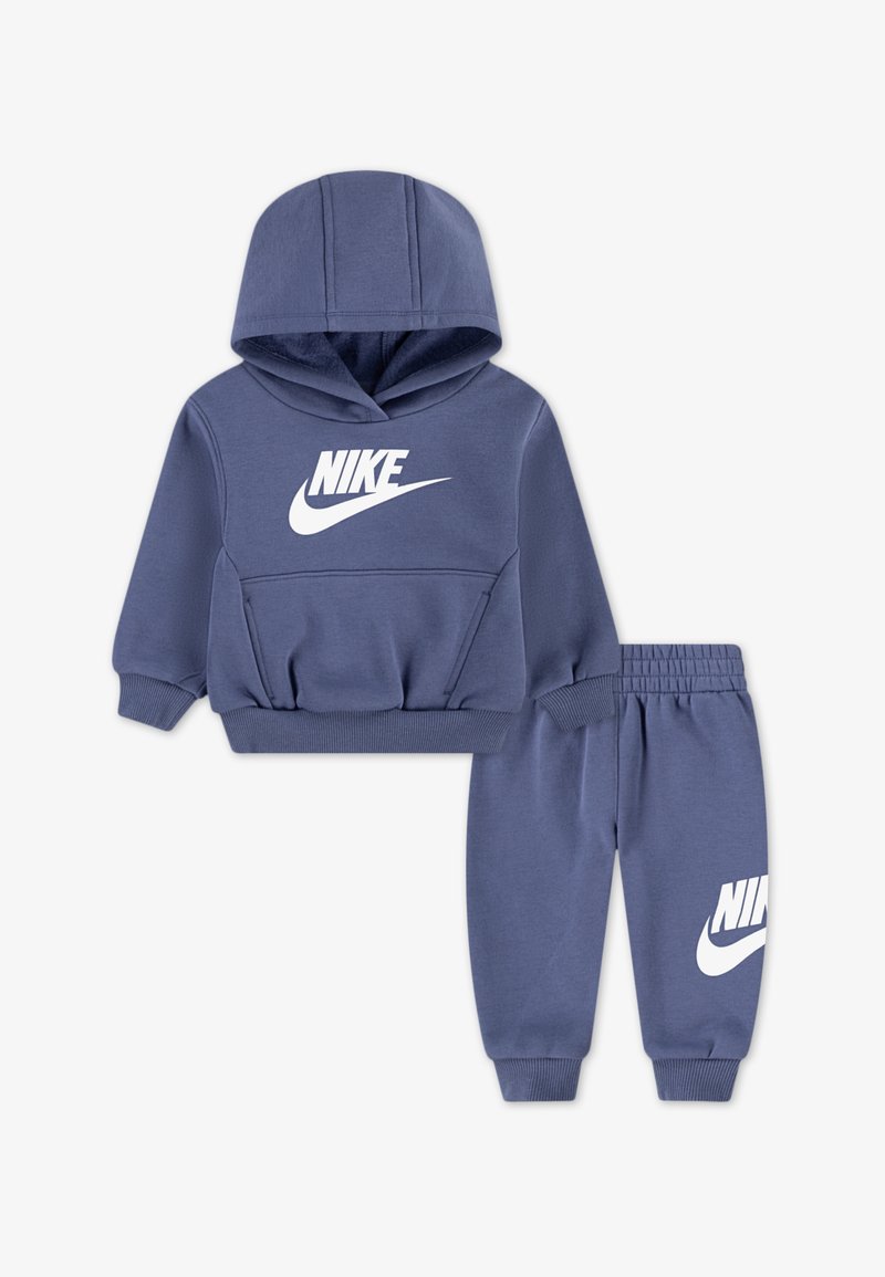 Set od dukserice i trenirki u tamnoplavoj boji, izrađen od mekanog materijala, sa velikim bijelim Nike logotipom na prednjoj strani i lijevoj nogavici.