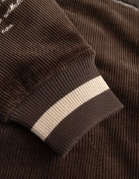 Brun ribbad tyg med en texturerad yta, med en mudd som har en bred krämfärgad rand för kontrast. Mjuk och åtsittande design.