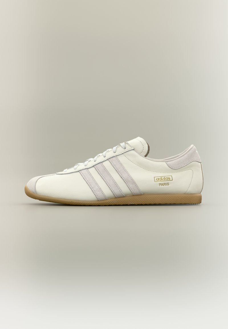 Λευκό δερμάτινο αθλητικό παπούτσι με τρεις απαλές μωβ ρίγες, λαστιχένια σόλα, στρογγυλεμένη μύτη και χρυσό έμβλημα με την επιγραφή "adidas PARIS" στη πλευρά.