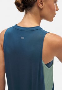 Top deportivo sin mangas en azul oscuro y verde. Tela suave y ligera con un detalle de logo en la parte trasera y un corte relajado para mayor comodidad.