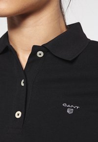 Polo noir en tissu texturé, avec un col classique et des boutons de couleur claire. Logo GANT brodé sur la poitrine.