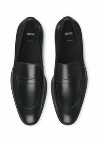 Mocassins en cuir noir avec une finition lisse, un bout arrondi et un subtil détail de couture sur le devant. Marque visible à l'intérieur.