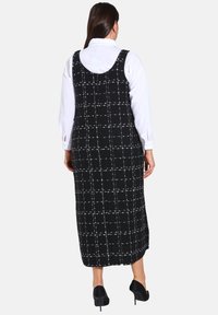Robes longues à carreaux noirs et blancs avec un dos dégagé, en tissu texturé ; portées sur une chemise blanche, assorties à des talons noirs.