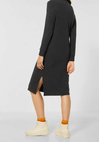 Langärmeliges, dunkelgraues Kleid aus weichem Stoff mit seitlichen Schlitzen, getragen mit cremefarbenen High-Top-Sneakern und orangefarbenen Socken.