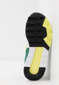 La suola delle scarpe è in gomma nera con battistrada triangolare, un accento giallo e una intersuola bianca texturizzata, etichettata con "Saucony" e "TR12."