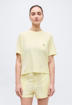 Woman wearing yellow and white vertical striped short-sleeve shirt and matching shorts, standing against a plain light background.