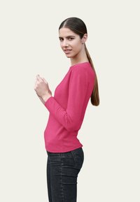 Pull en maille rose ajusté à manches longues avec un col rond, associé à un jean en denim foncé. Texture lisse et design décontracté.