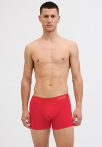 Rote Baumwoll-Boxershorts mit einem breiten Bund, auf dem das Logo "JACK & JONES" abgebildet ist. Der Stoff ist glatt, hat eine körpernahe Passform und keine sichtbaren Muster.