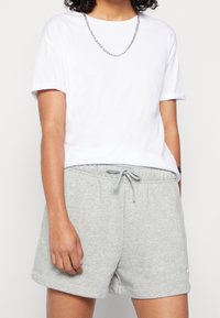 Bílá bavlněná trička s ohrnutými rukávy, spárovaná se šedými bavlněnými šortkami s elastickým pasem a tkaničkou, a malým logem.