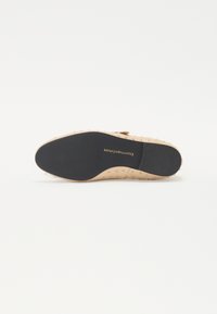 Scarpa slip-on nuda con superficie strutturata e dettagli borchiati. Suola in gomma nera con logo. Design liscio e pulito senza lacci visibili.