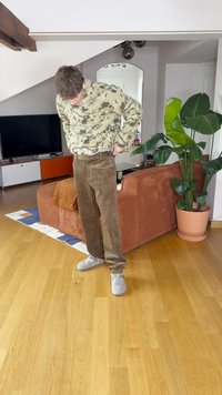 Rjavi kordurojske hlače s ravnimi nogavicami, teksturirano blago in subtilen rebrast vzorec. V kombinaciji z zgornjim delom v zeleni in bež vzorcu.